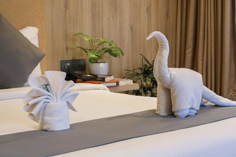 Swan-shaped towels on a guest room bed with grey pillows and a wooden headboard