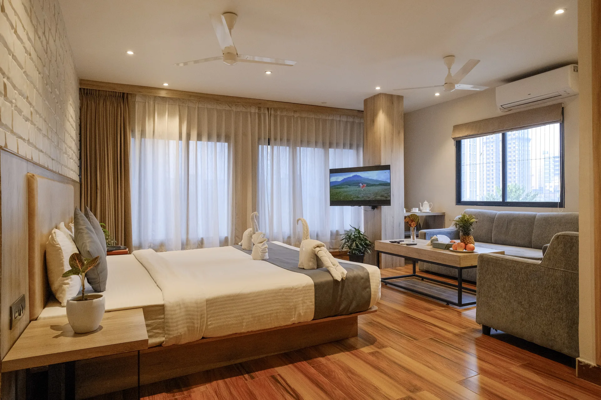 Luxury suite with a double bed, sofa and large windows at Firangipani Ecosuites in New Town, Kolkata